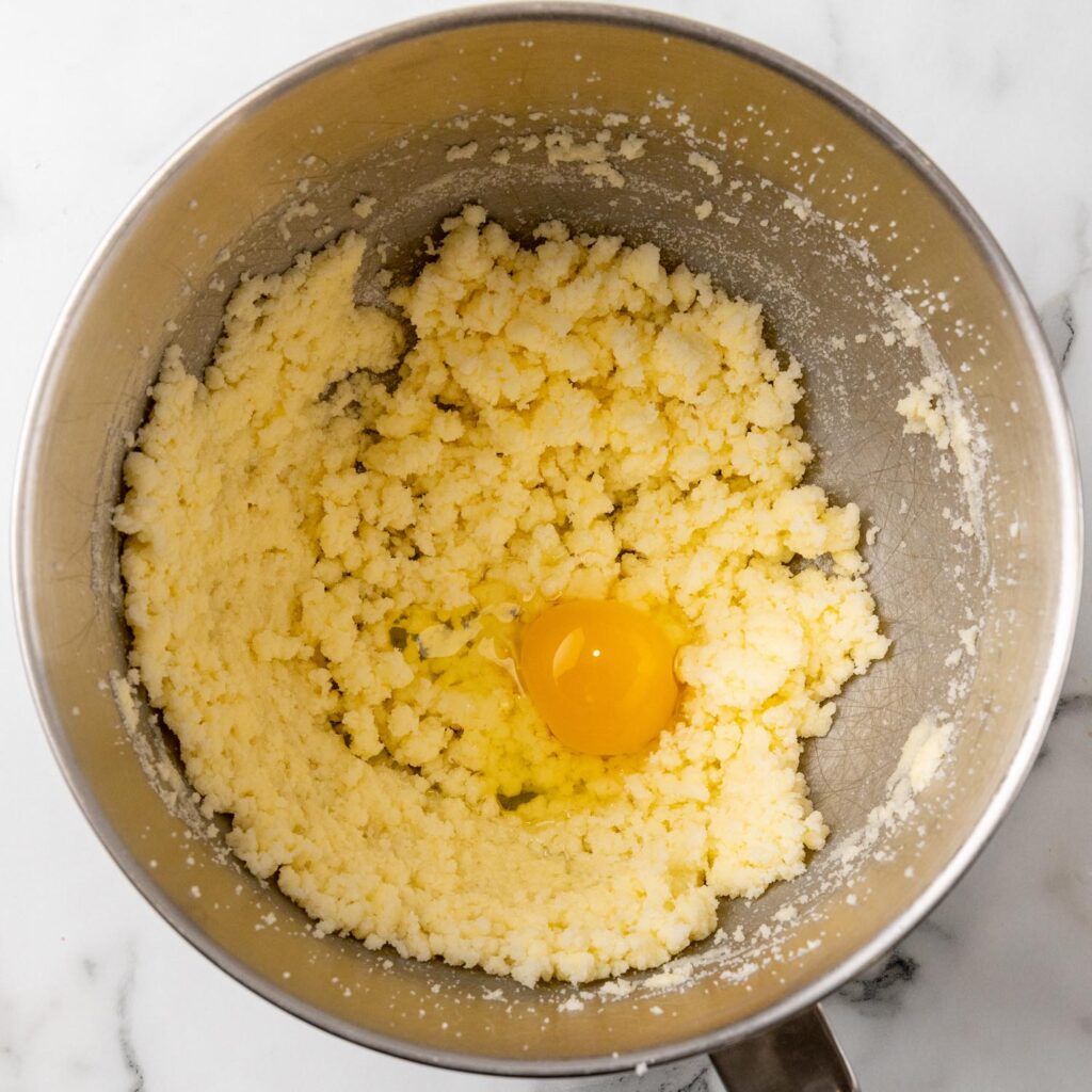 creamed butter and sugar in a metal bowl with a cracked egg added.