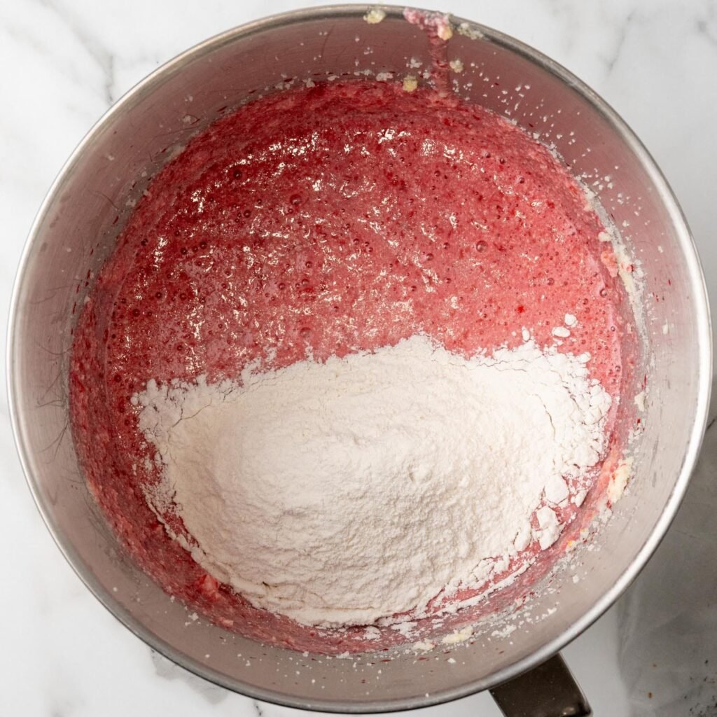 Dry ingredients added to wet ingredients to make strawberry cake in a metal mixing bowl.
