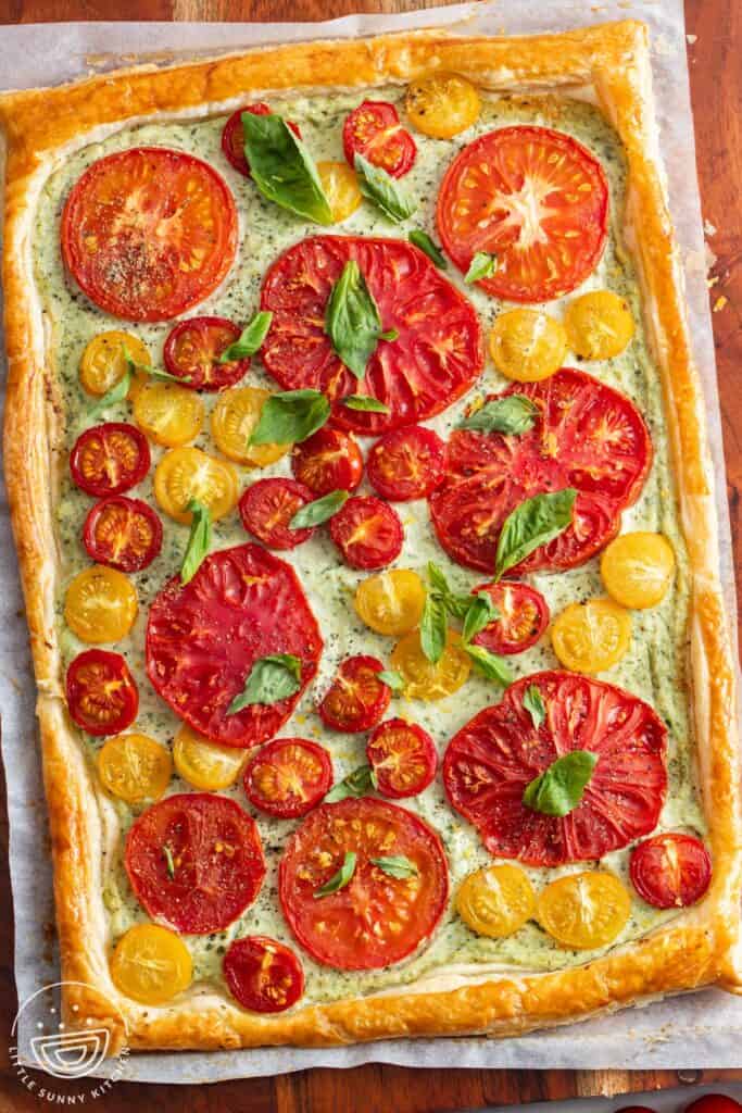 Tomato tart baked with puff pastry and ricotta cheese. The baked tomatoes are topped with fresh basil leaves, salt, and pepper.