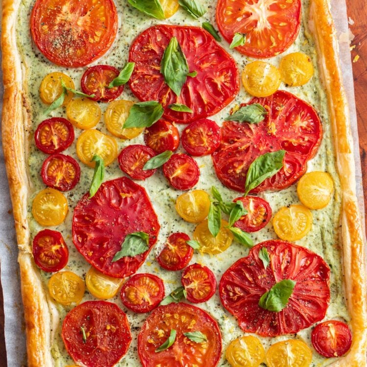 Tomato tart baked with puff pastry and ricotta cheese. The baked tomatoes are topped with fresh basil leaves, salt, and pepper.