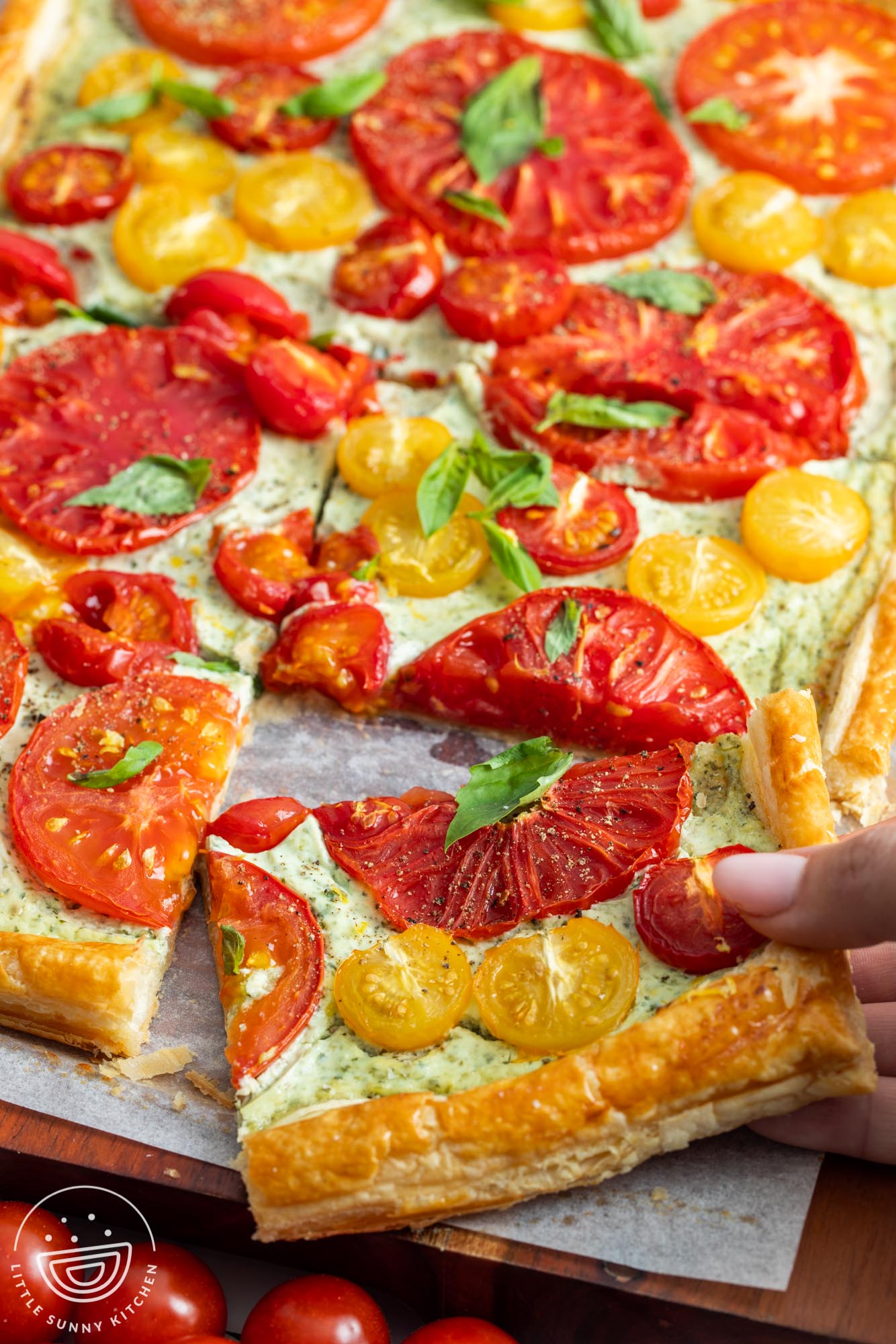 a tomato tart cut into squares. a hand is picking up a corner piece.