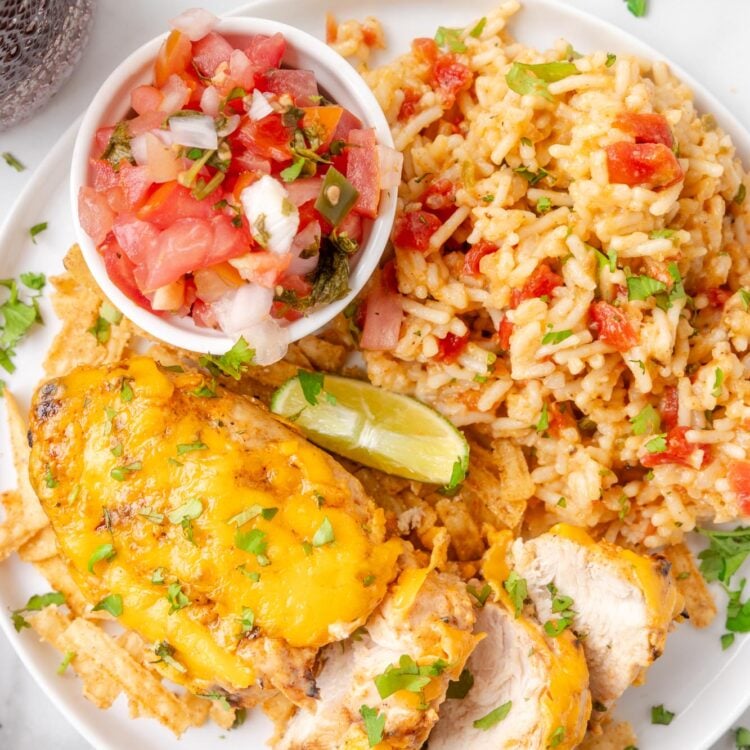 a white plate of sliced fiesta lime chicken, spanish rice, a lime wedge and a small bowl of pico de gallo.