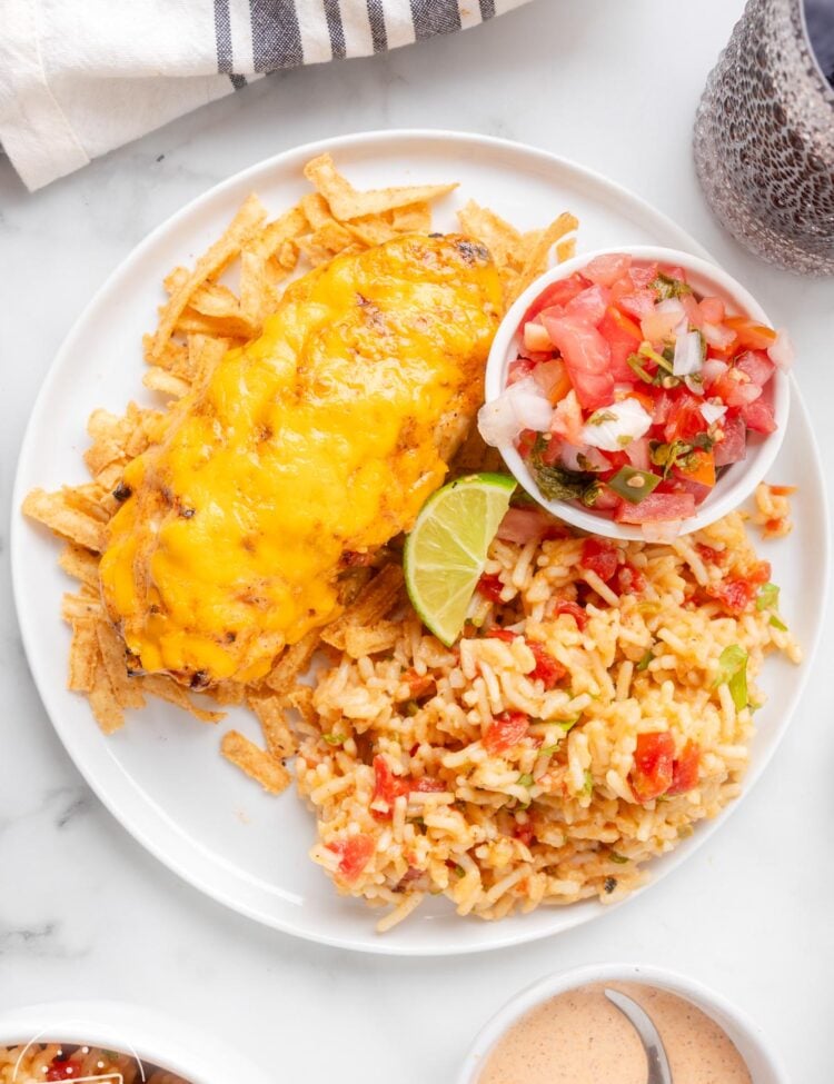 a white plate of cheesy fiesta lime chicken, spanish rice, and pico de gallo.