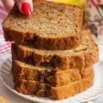 four slices of banana bread stacked on a plate. A hand is removing the top slice.