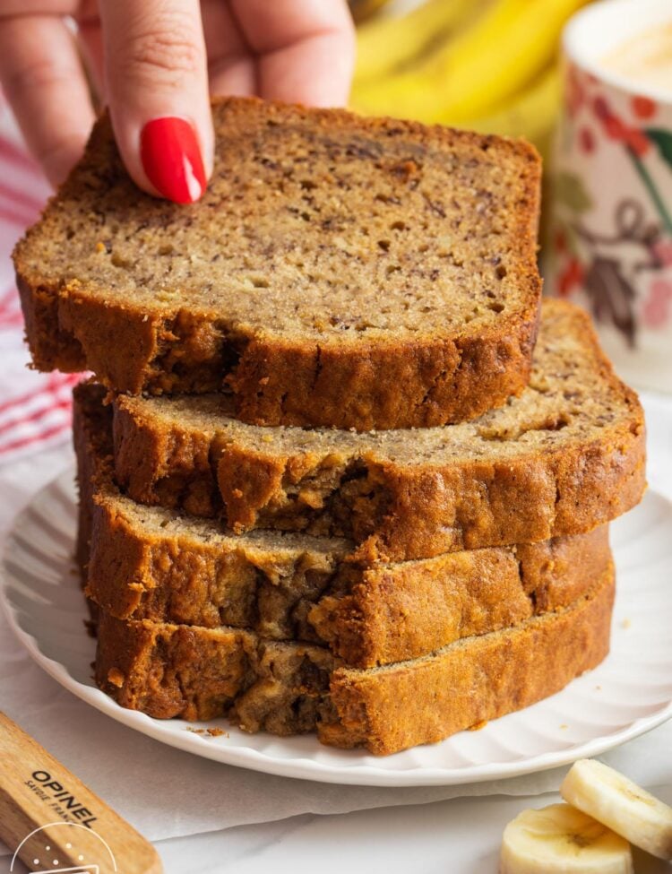 four slices of banana bread stacked on a plate. A hand is removing the top slice.