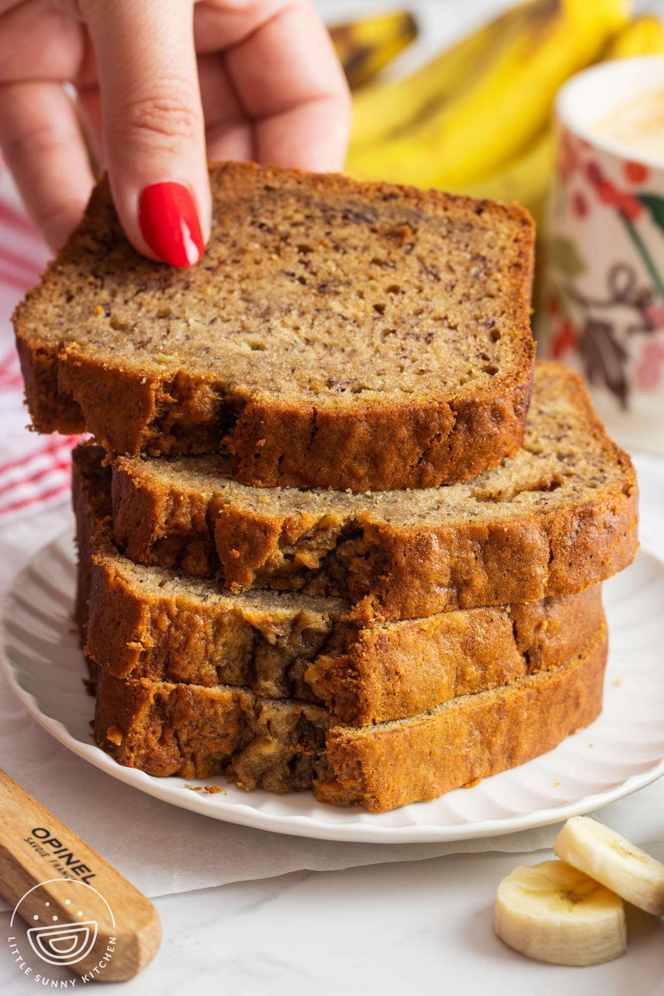 four slices of banana bread stacked on a plate. A hand is removing the top slice.