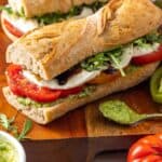 two homemade caprese sandwiches with sliced tomatoes, arugula, balsamic glaze, and sliced cheese.