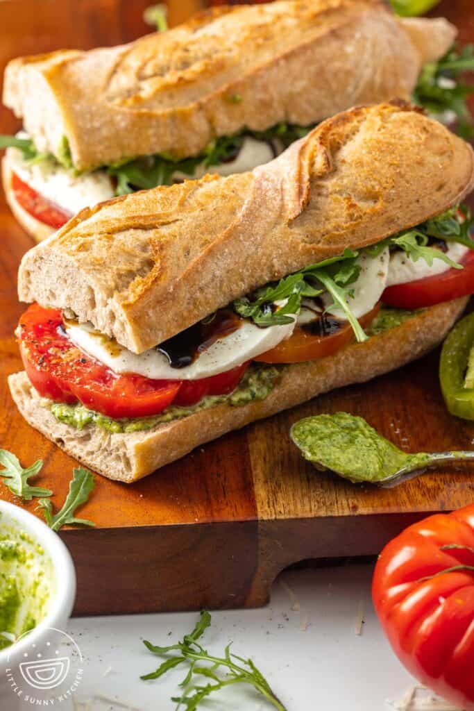 two homemade caprese sandwiches with sliced tomatoes, arugula, balsamic glaze, and sliced cheese.