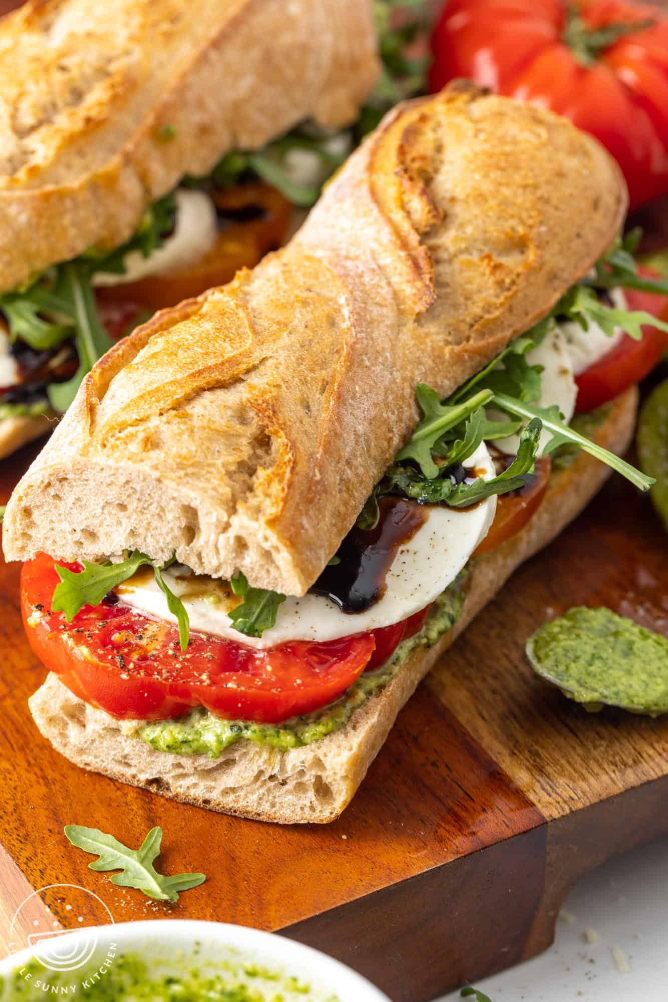 half french baguette layered with pesto, tomatoes, and mozzarella to make a caprese sandwich.