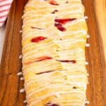 a cherry danish braid on a wooden cutting board, drizzled with icing.