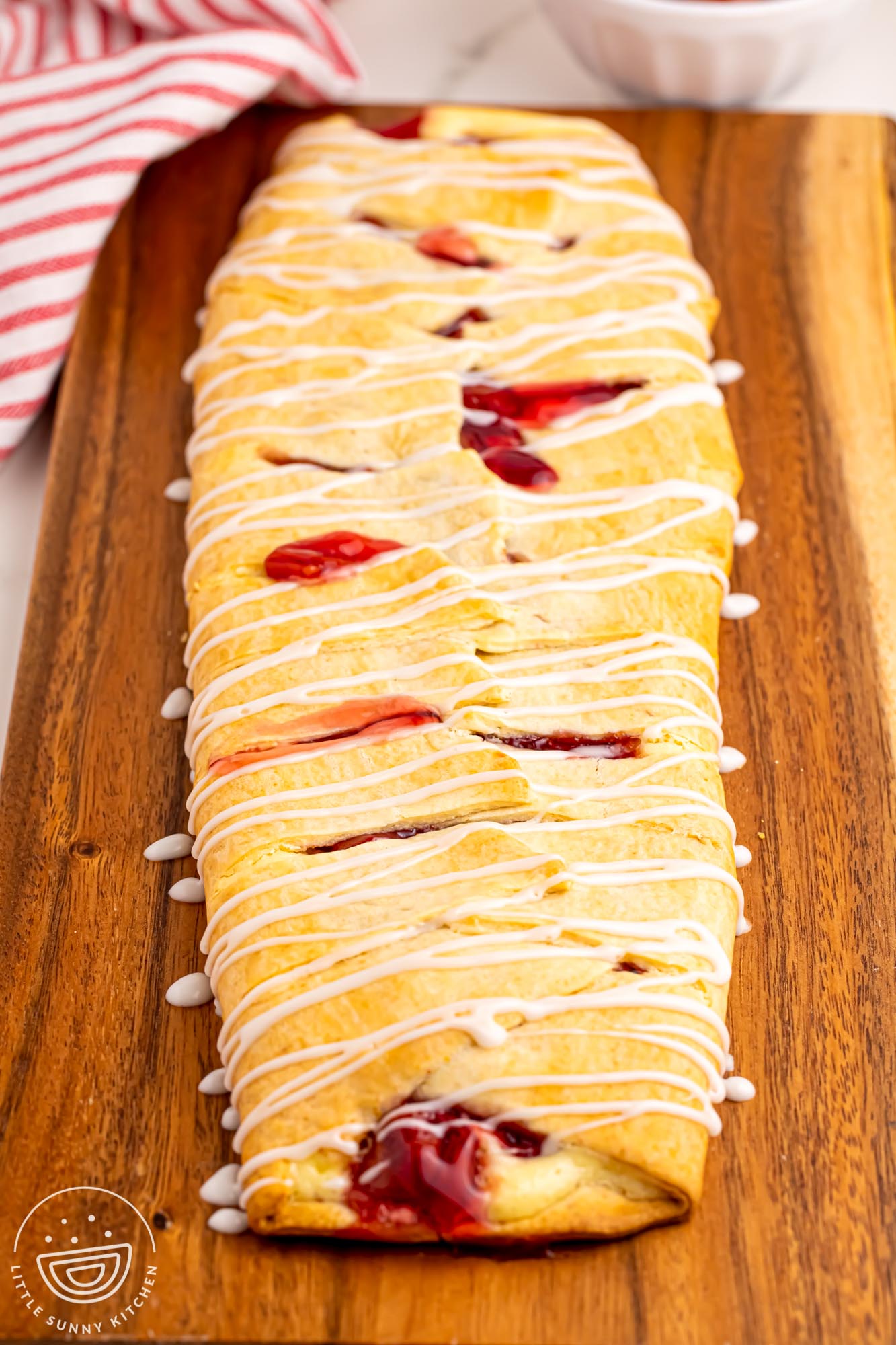 a cherry danish braid on a wooden cutting board, drizzled with icing.