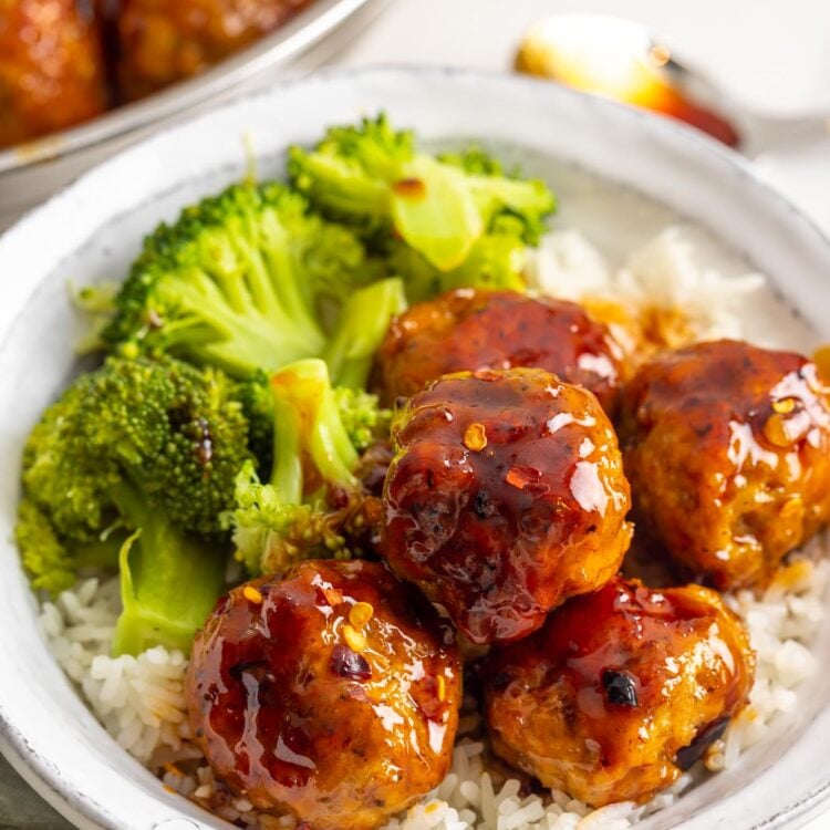a rustic white ceramic plate of rice topped with spicy chicken meatballs with a side of broccoli.