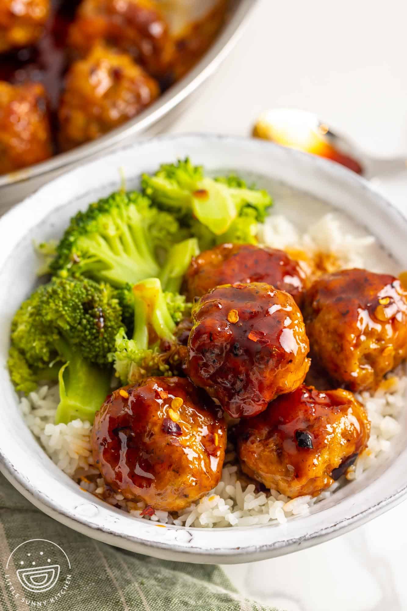 a rustic white ceramic plate of rice topped with spicy chicken meatballs with a side of broccoli.