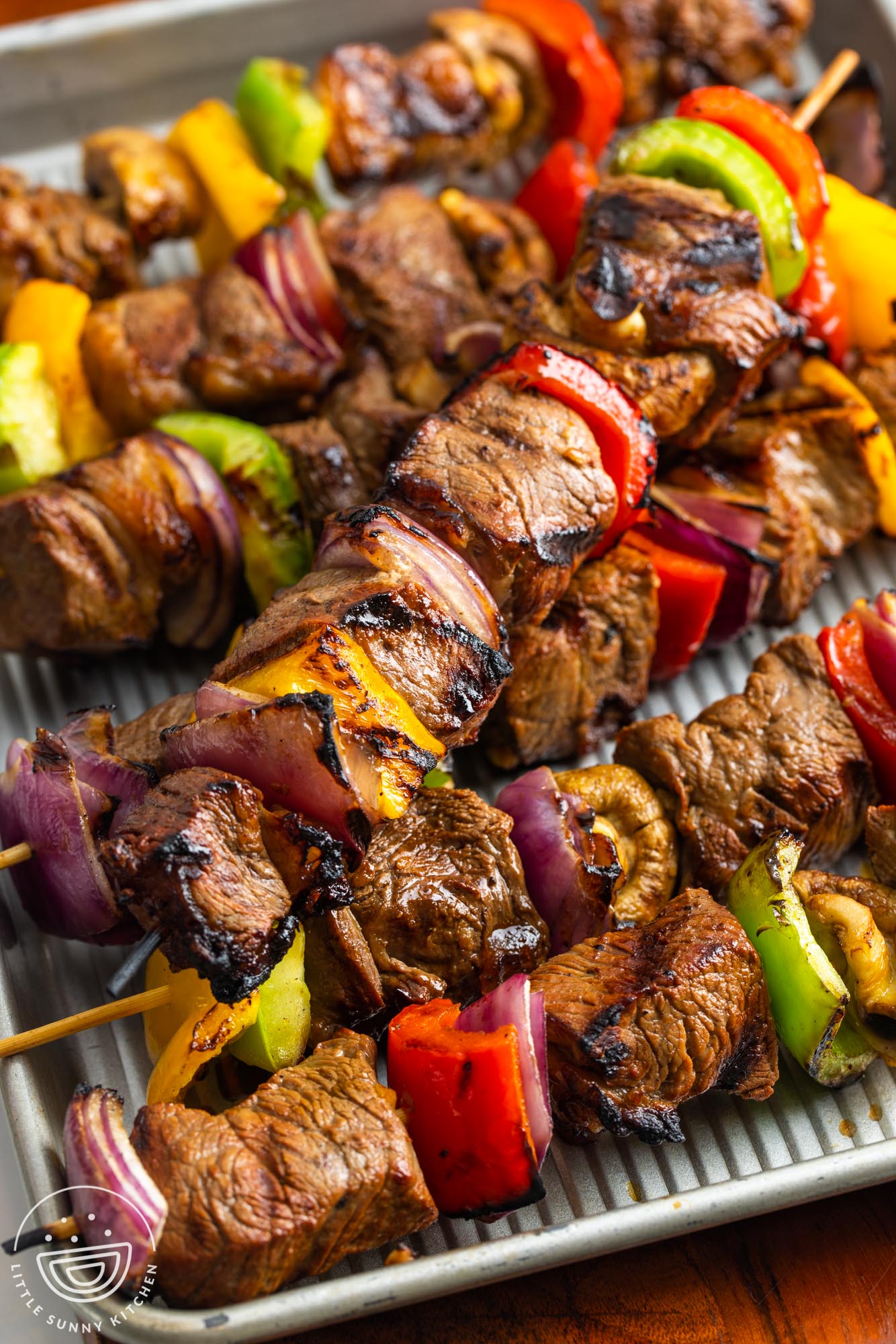 cooked grilled beef kabobs on a metal sheet pan, resting.