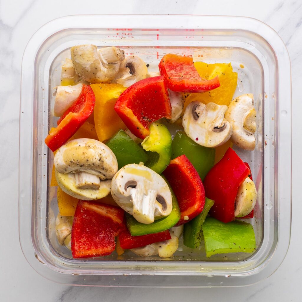 cubed bell peppers and halved mushrooms marinating in a plastic container.