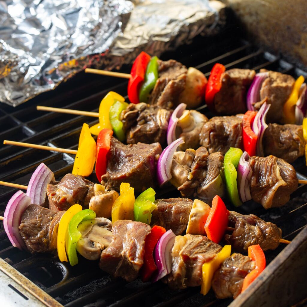 skewers of beef, mushrooms, peppers, and onions on an outdoor grill.