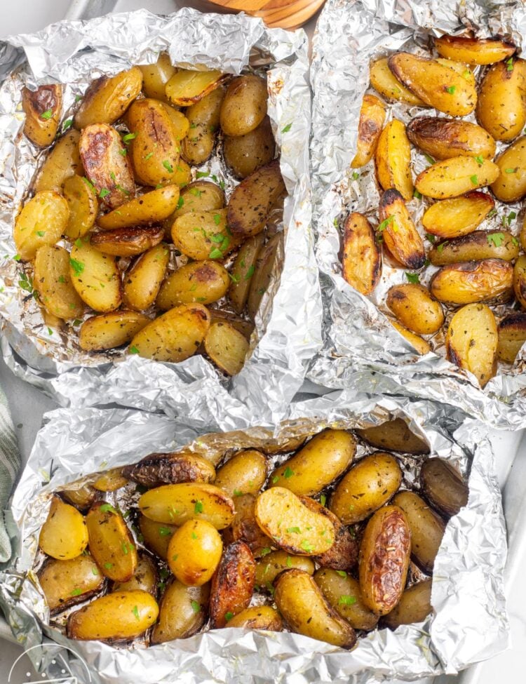 three foil packets filled with new potatoes cut in half and roasted.