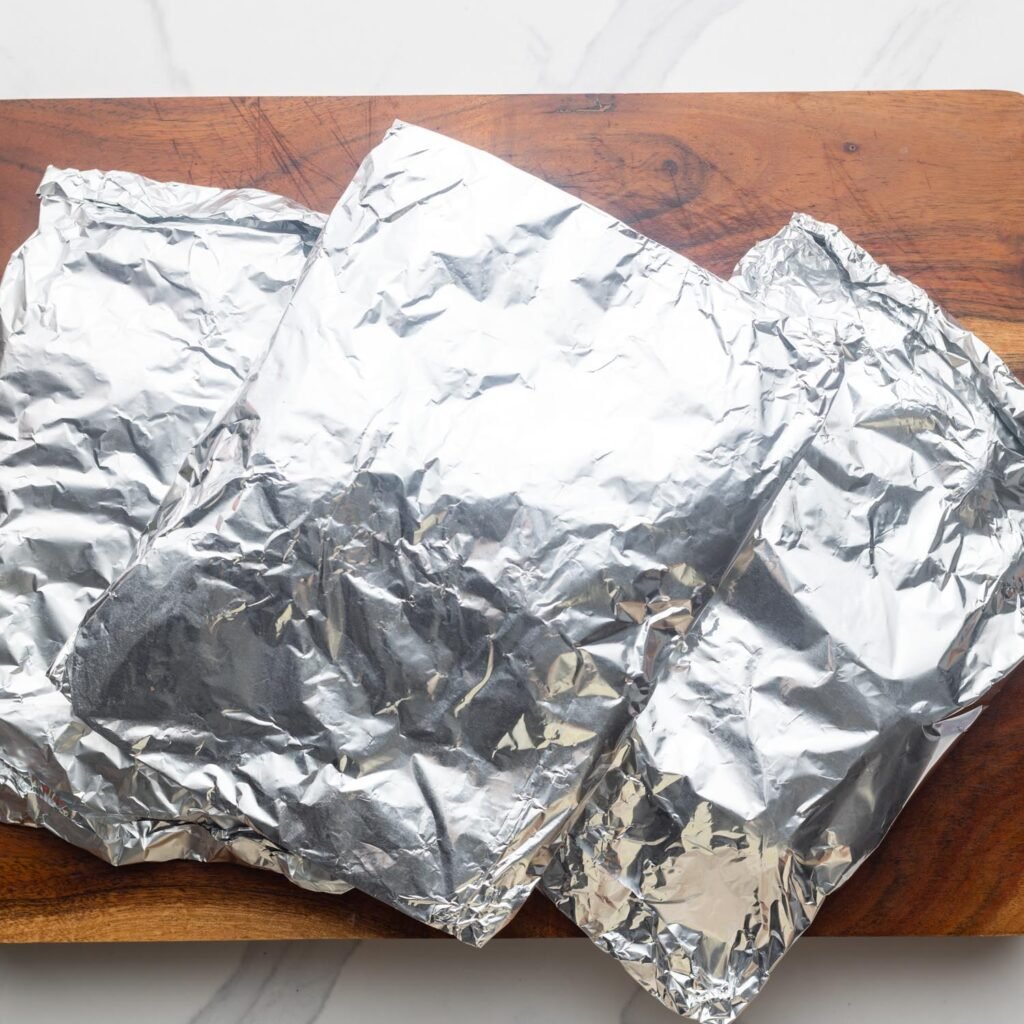 foil packets on a wooden cutting board.