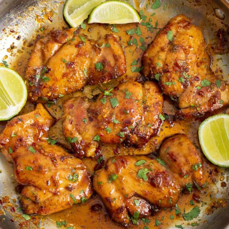 honey lime chicken garnished with cilantro and lime wedges, in a stainless steel skillet, viewed from above.