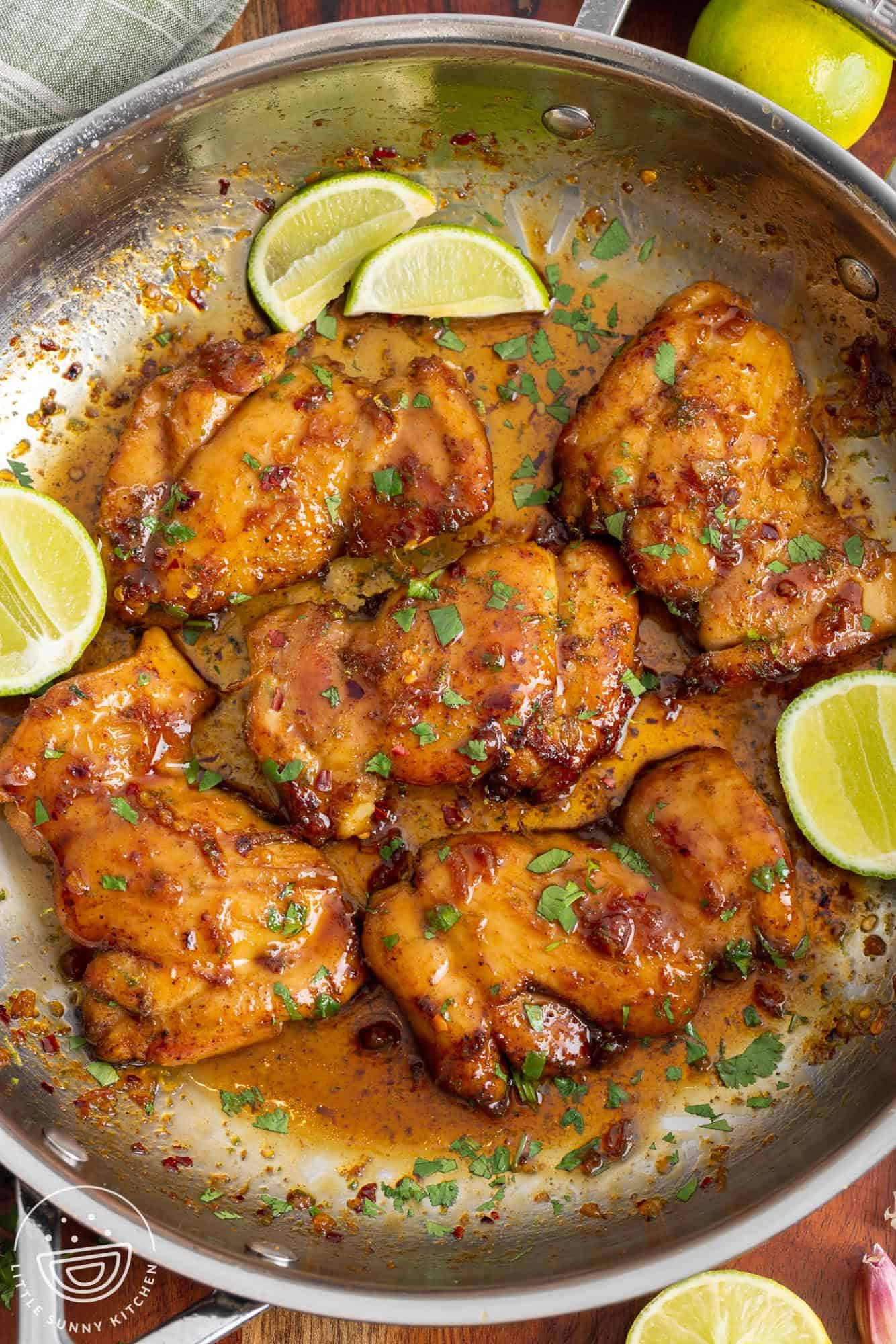 honey lime chicken garnished with cilantro and lime wedges, in a stainless steel skillet, viewed from above.