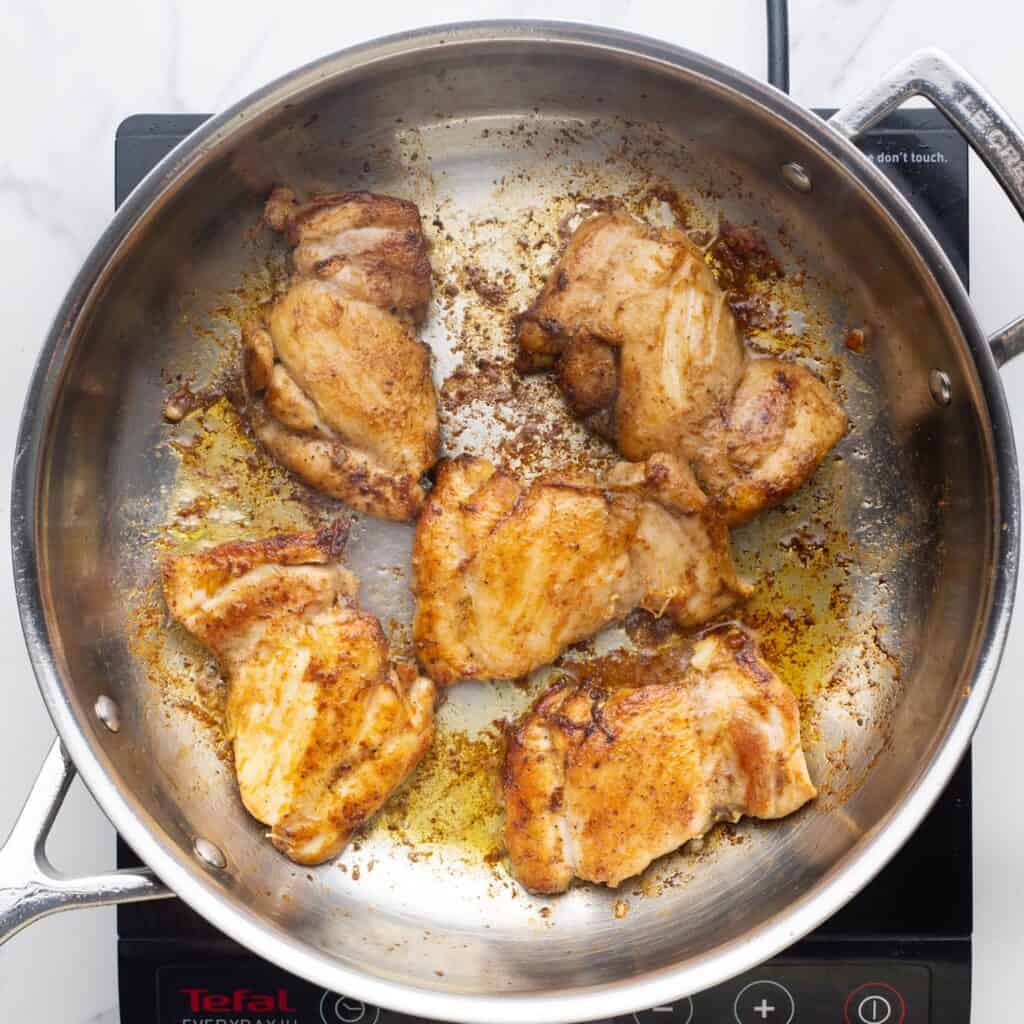 boneless chicken thighs cooking in a stainless steel skillet over an electric burner.