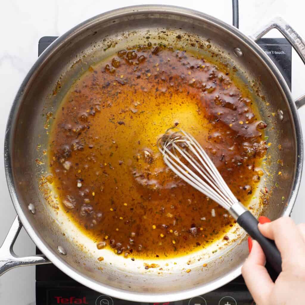 honey lime sauce for chicken cooking down in a stainless steel skillet, with a small whisk.