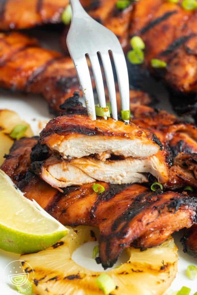a fork holding a sliced piece of grilled huli huli chicken .