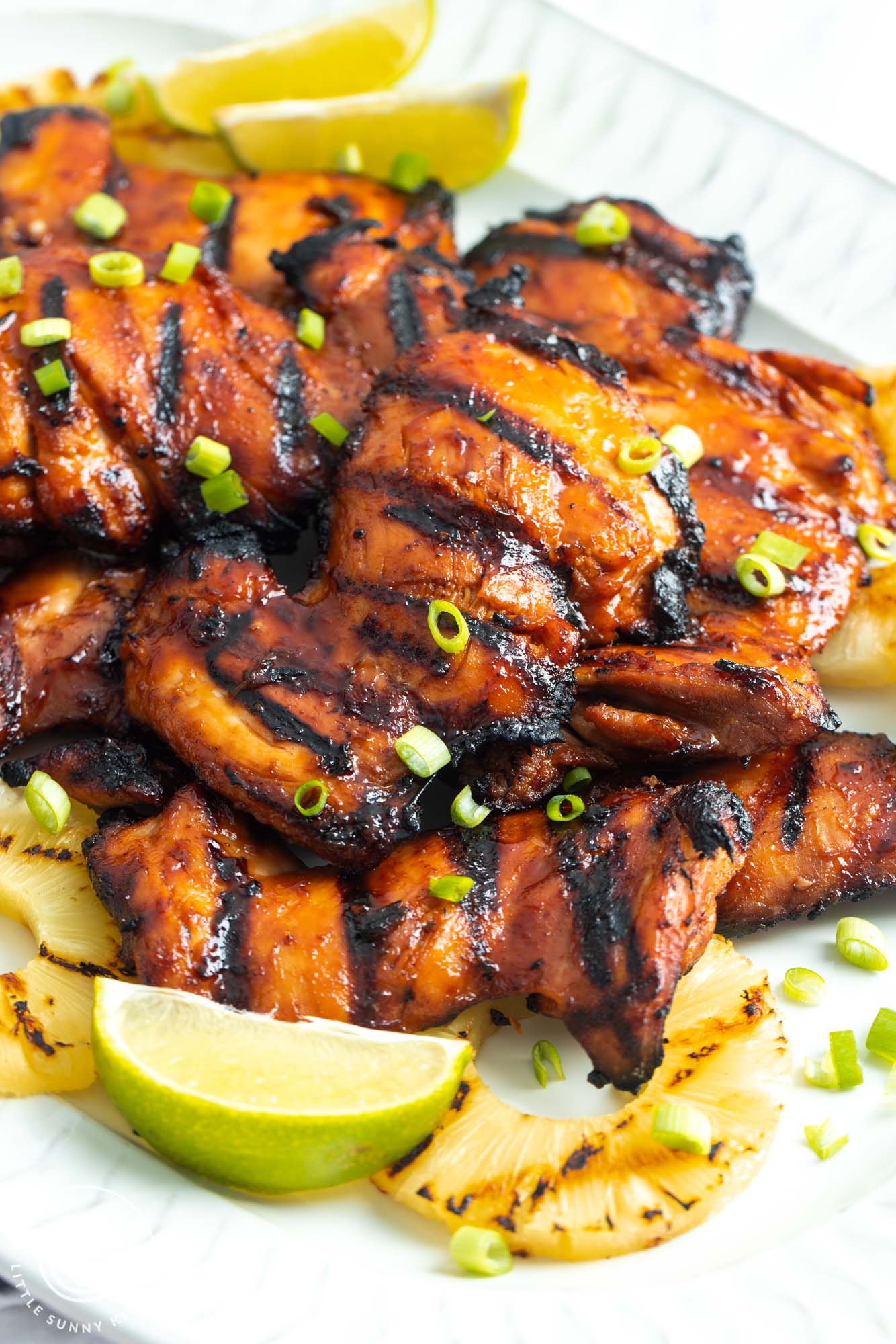 grilled hawaiian chicken on a platter with sliced green onions, lime wedges, and grilled pineapple.