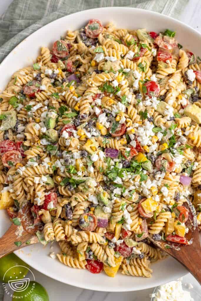 a large white bowl of rotini pasta salad with vegetables, beans, cilantro and cotija cheese.