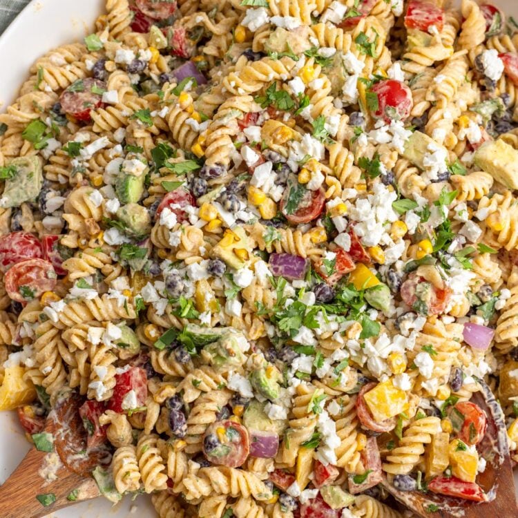 a large white bowl of rotini pasta salad with vegetables, beans, cilantro and cotija cheese.