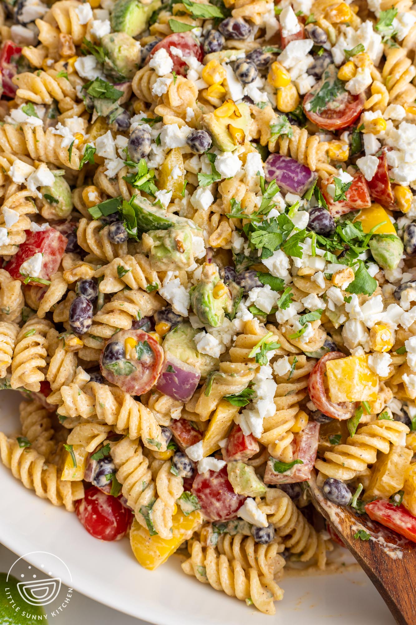 closeup of Mexican pasta salad. Rotini pasta in a creamy sauce with chopped bell peppers, avocado, tomatoes, corn, black beans, and crumbled cheese.