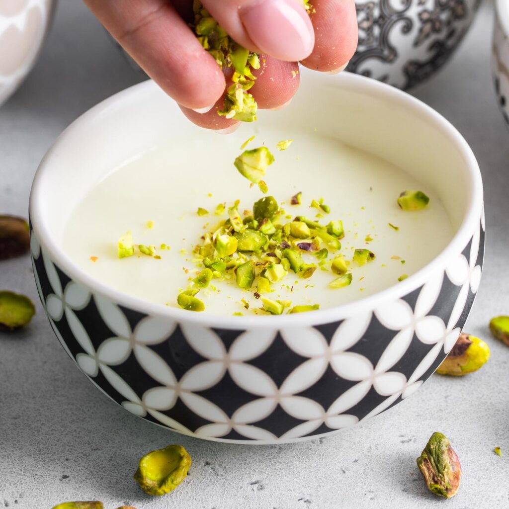 Mouhalabieh in a bowl being garnished with crushed pistachios