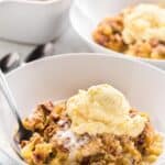 a scoop of warm pineapple dump cake topped with a scoop of ice cream in a white bowl with a spoon.