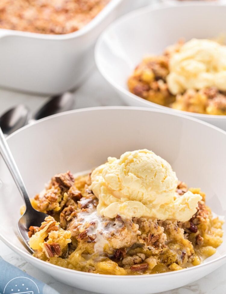 a scoop of warm pineapple dump cake topped with a scoop of ice cream in a white bowl with a spoon.