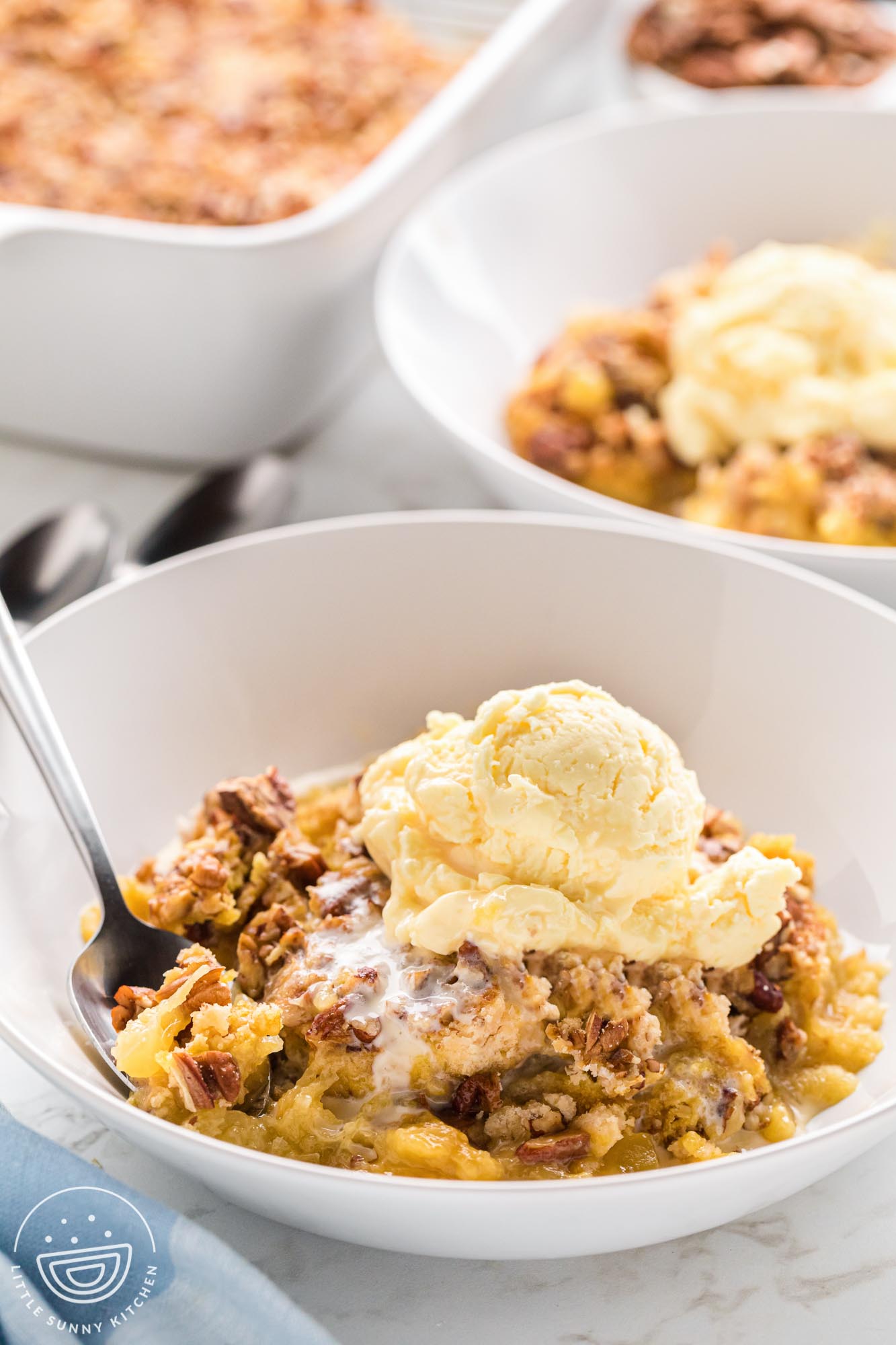 a scoop of warm pineapple dump cake topped with a scoop of ice cream in a white bowl with a spoon.
