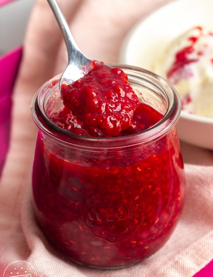 a small rounded weck jar of raspberry compote. A spoon is lifting out some of the sauce.