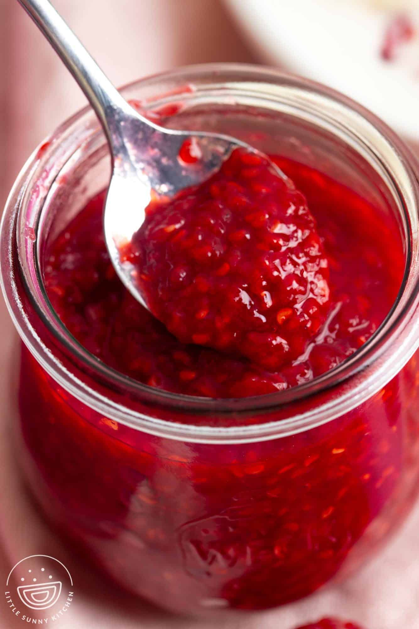 a small glass jar of raspberry compote with a teaspoon it it.