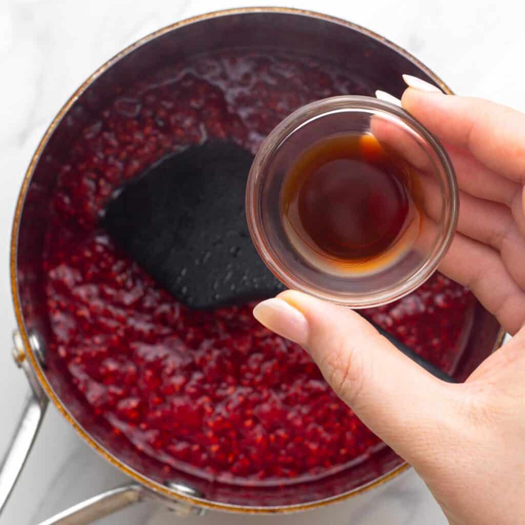 a hand adding vanilla to a pot of raspberry compote.