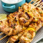 a small metal pan holding four salmon kabobs and a bowl of creamy salmon sauce.