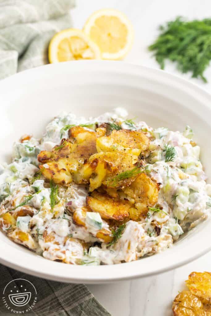 a serving bowl of smashed potato salad with dill, topped with crispy potato pieces.