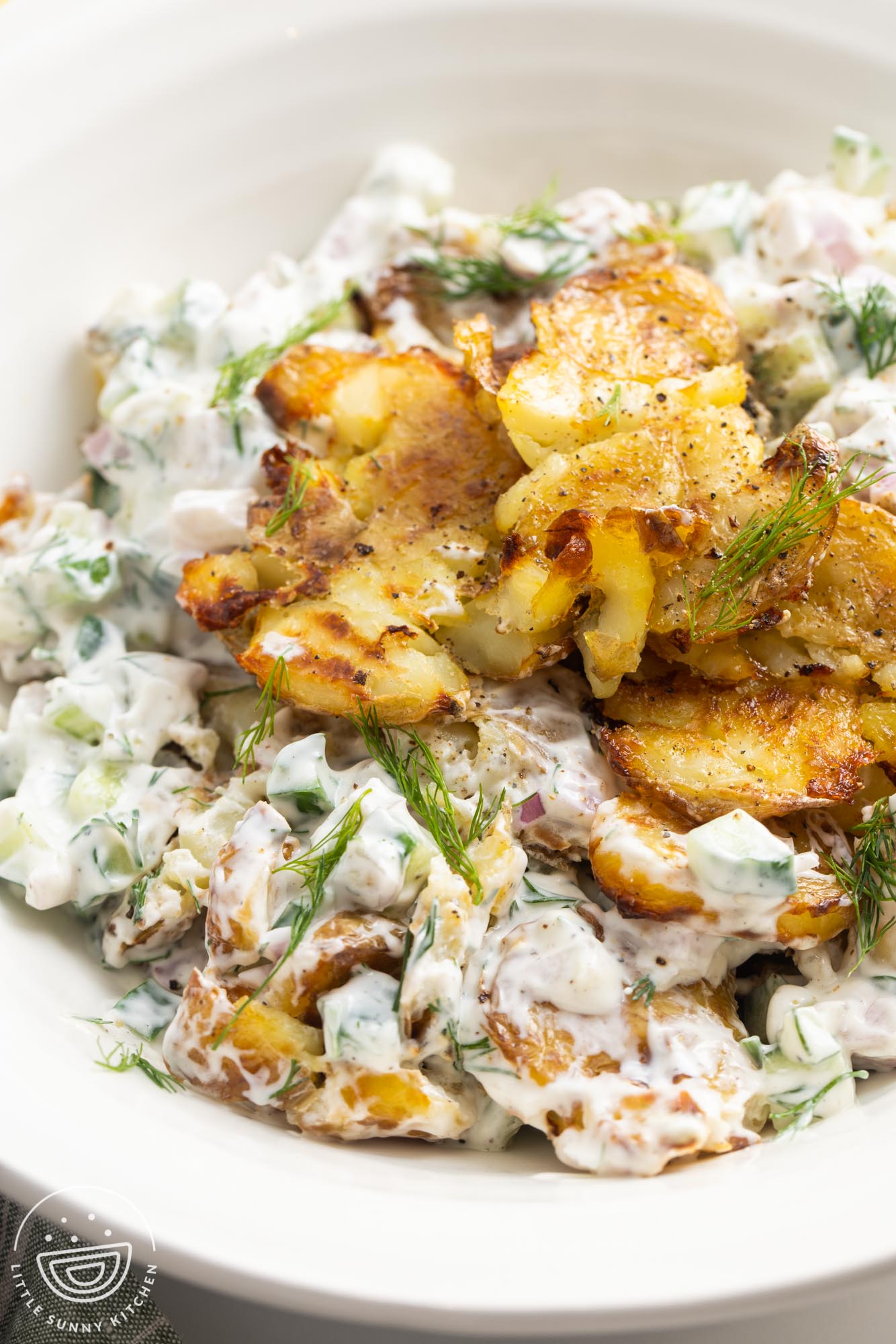 closeup of creamy tzatziki potato salad topped with crispy smashed potatoes and dill sprigs.