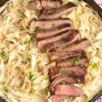 a skillet of homemade fettuccine alfredo topped with sliced seared steak.