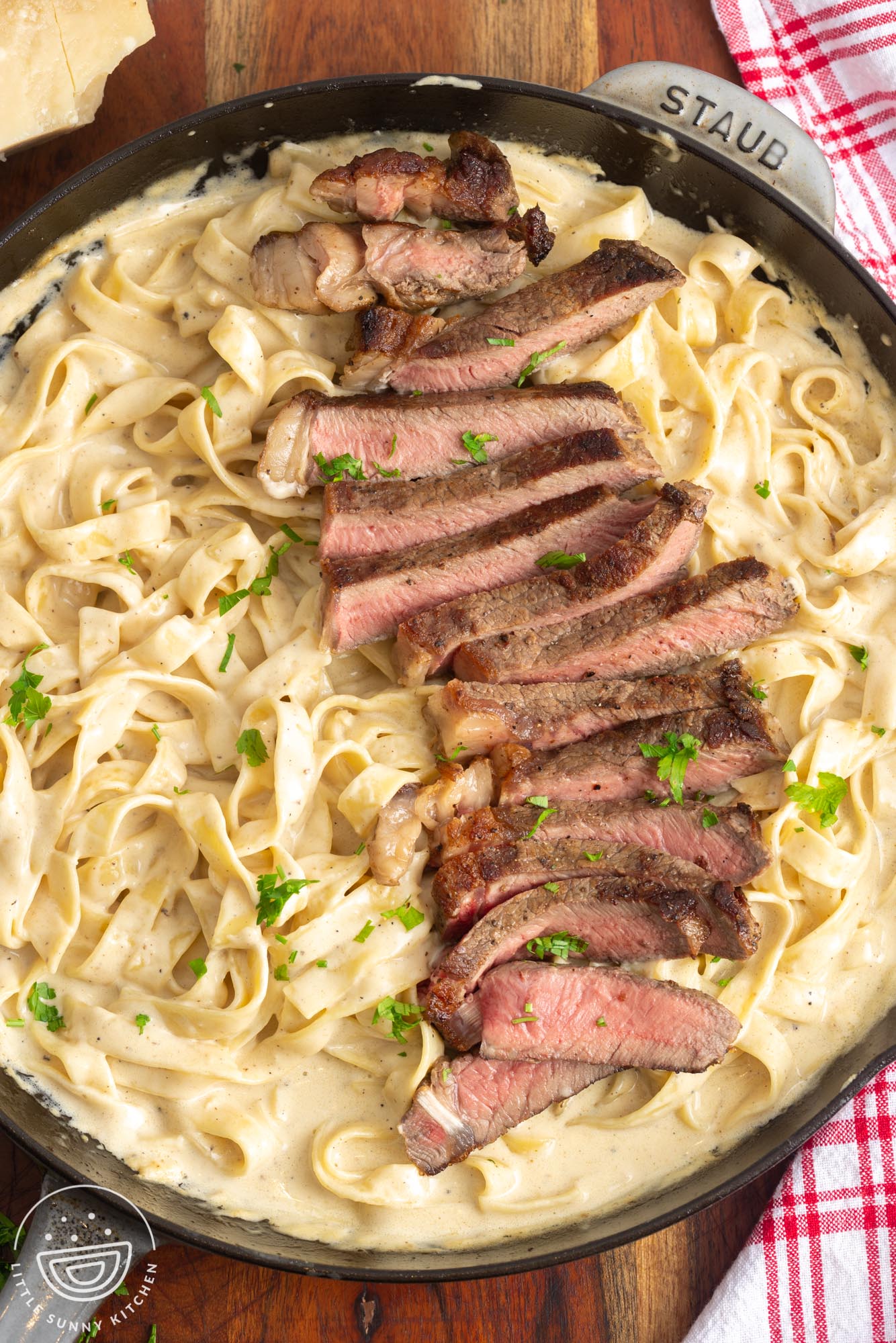 a skillet of homemade fettuccine alfredo topped with sliced seared steak.