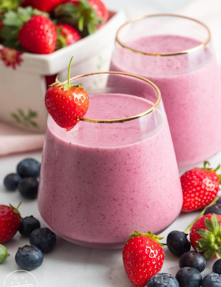 two wide glasses of berry smoothie. Around the glasses are fresh strawberries and blueberries.