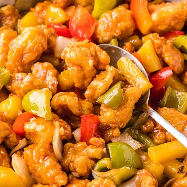 Sweet and Sour Chicken in a stainless steel skillet with a serving spoon