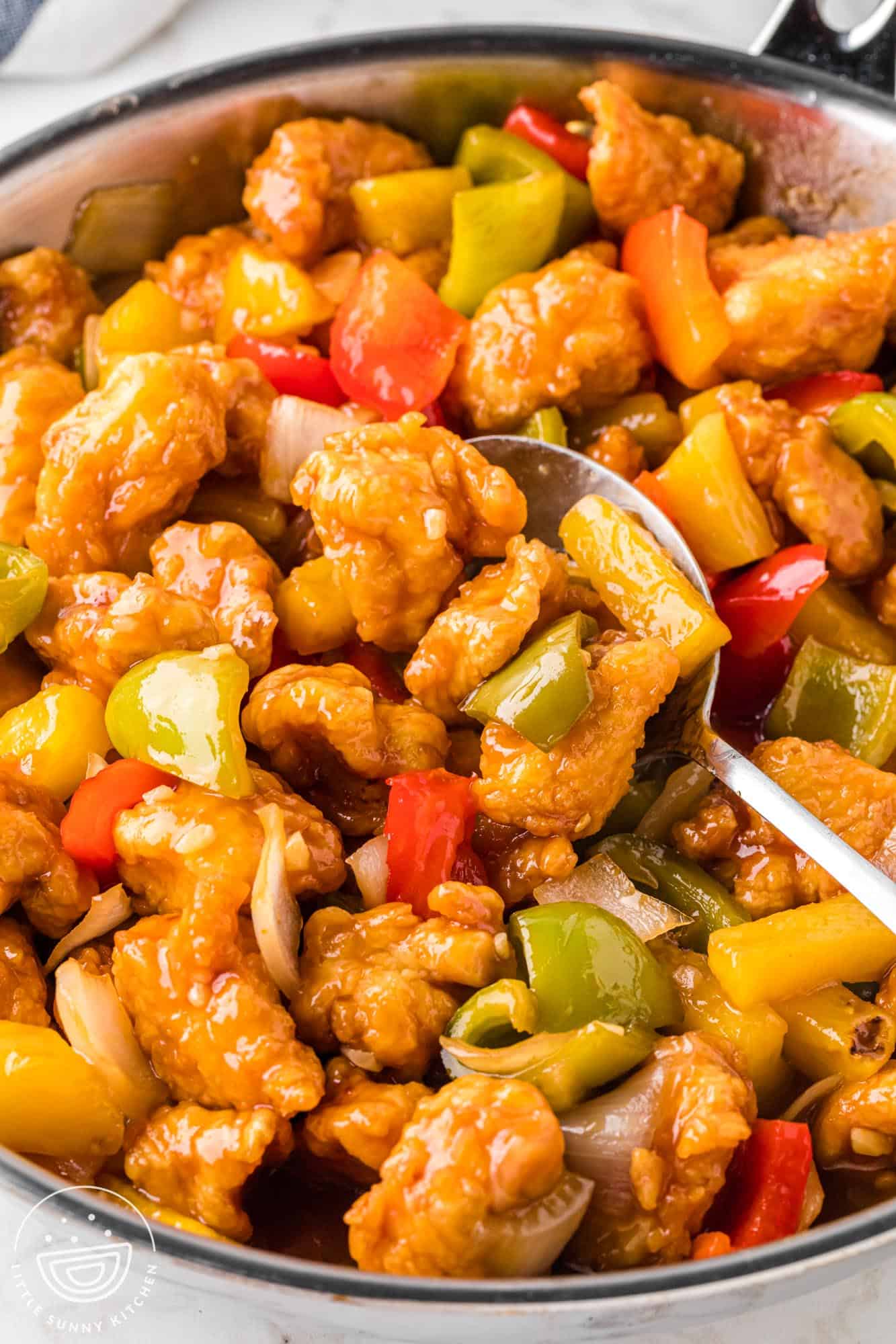 Sweet and Sour Chicken in a stainless steel skillet with a serving spoon