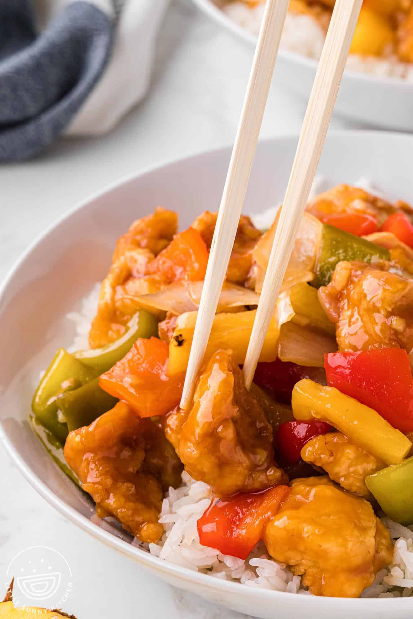 Chop sticks taking a piece of sweet and sour chicken from a bowl