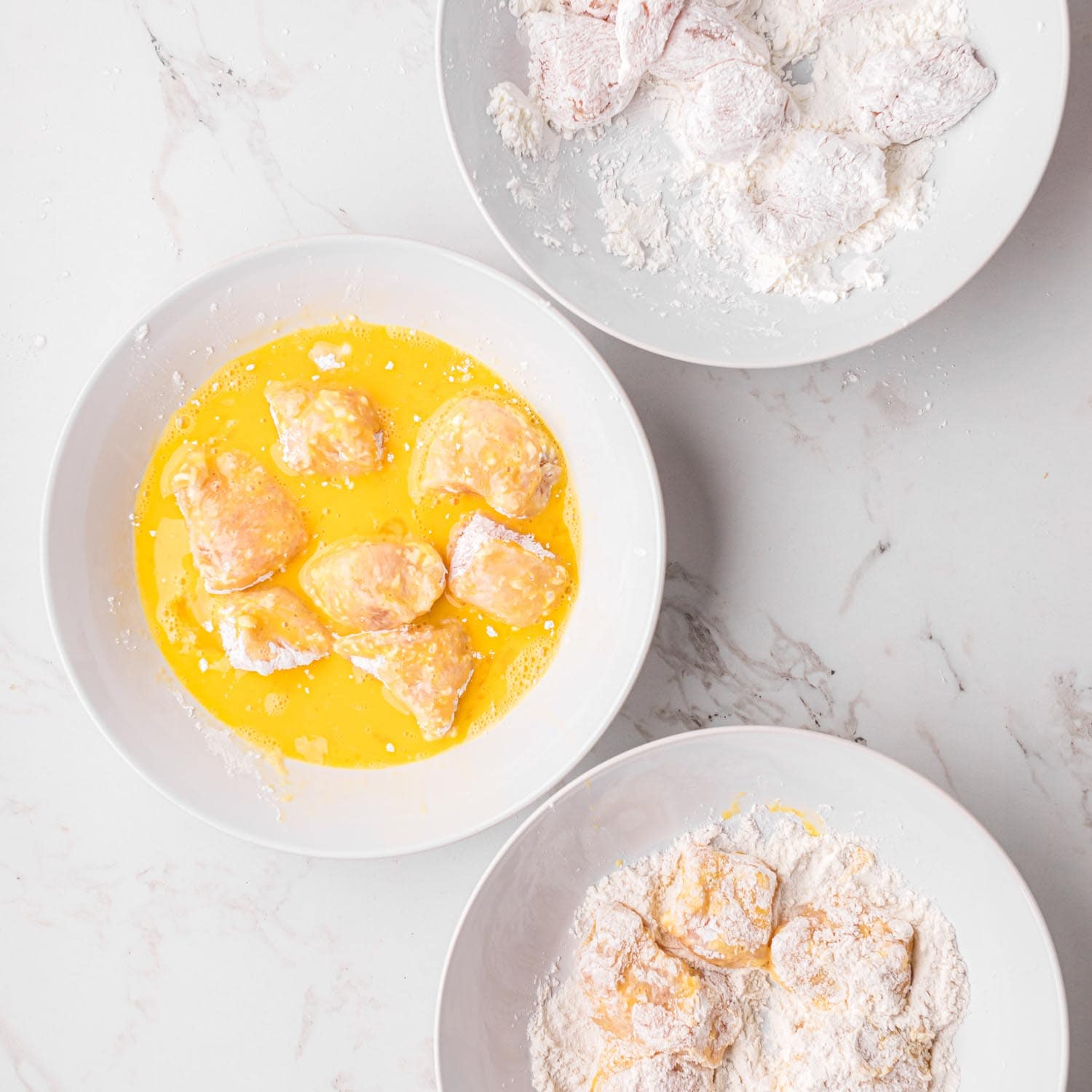 3 bowls of flour, egg, cornstarch with chicken being dredges in each.