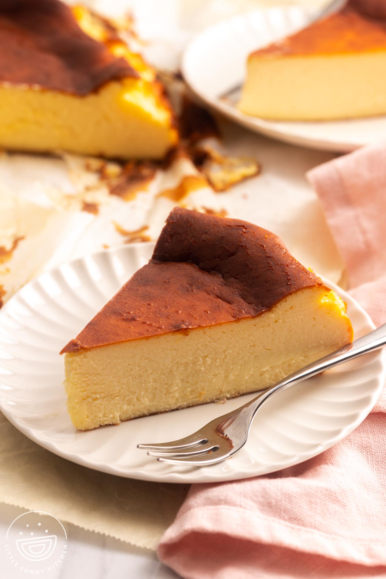 one slice of basque cheesecake on a white dessert plate with a small silver fork.