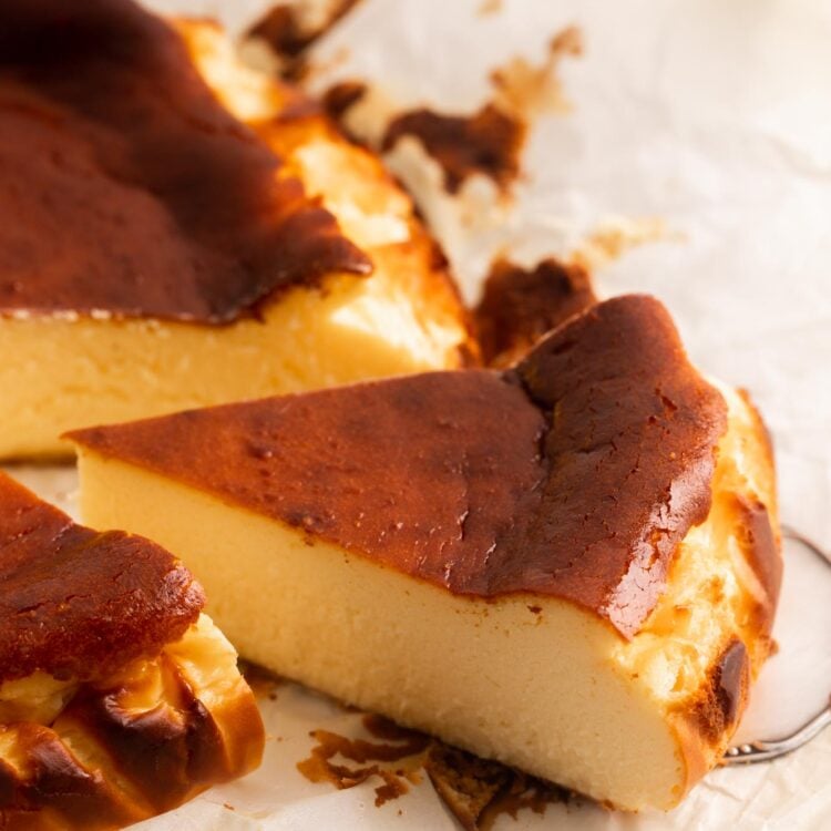 a slice of basque cheesecake with a caramelized brown top, pulled away from the whole cake with a cake server.